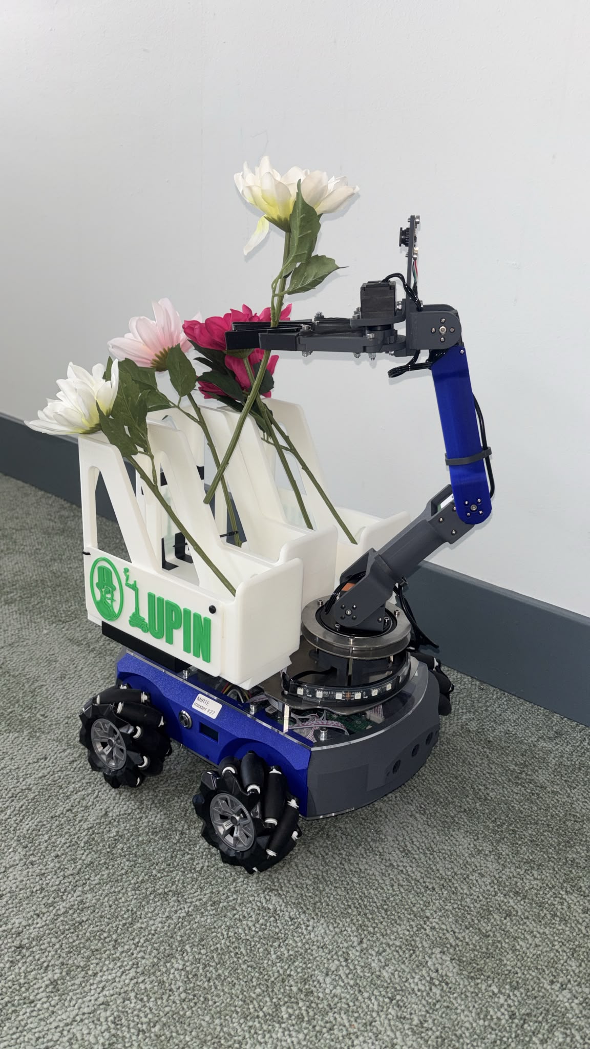 Lupin robot, front view: the 4-DOF arm raised with a flower in the gripper above its white 3D-printed crate